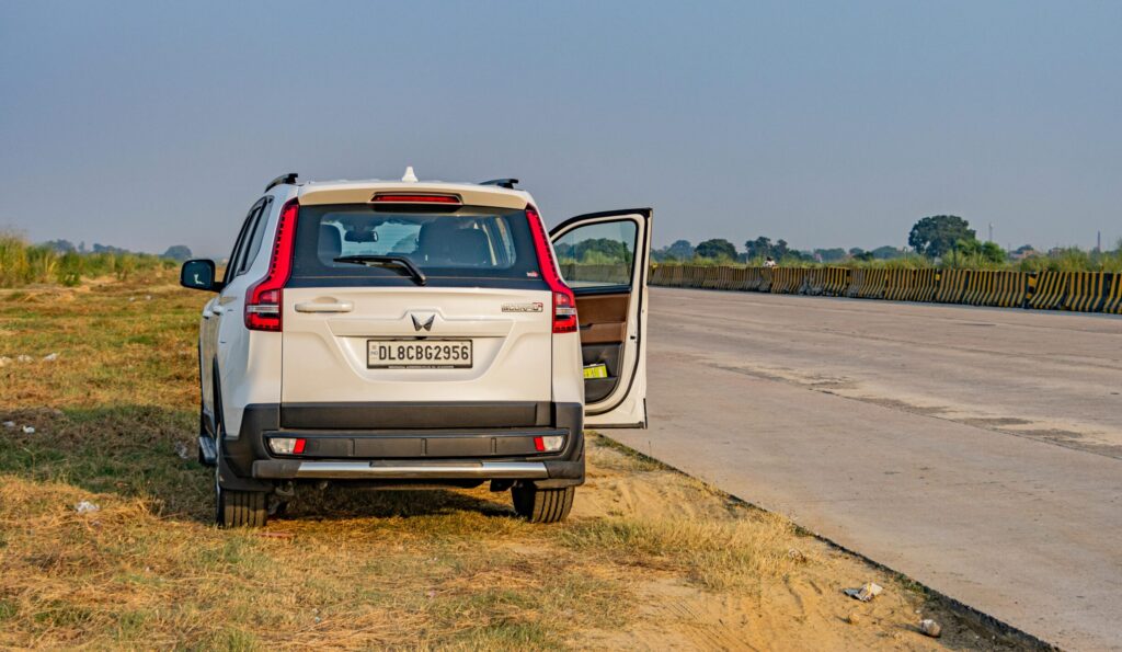 A white SUV parked on a deserted Indian highway during daytime, capturing the vast open road and landscape.